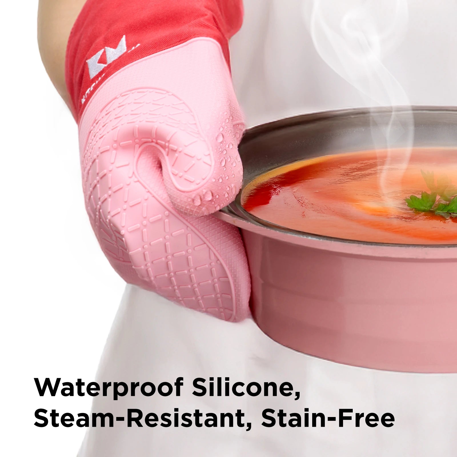 Close-up of a person holding a hot pot of tomato soup with red and pink Shopkitchenmama silicone oven mitts. The mitts show water droplets on the surface, highlighting their waterproof, steam-resistant, and stain-free features. Text overlay reads: "Waterproof Silicone, Steam-Resistant, Stain-Free."